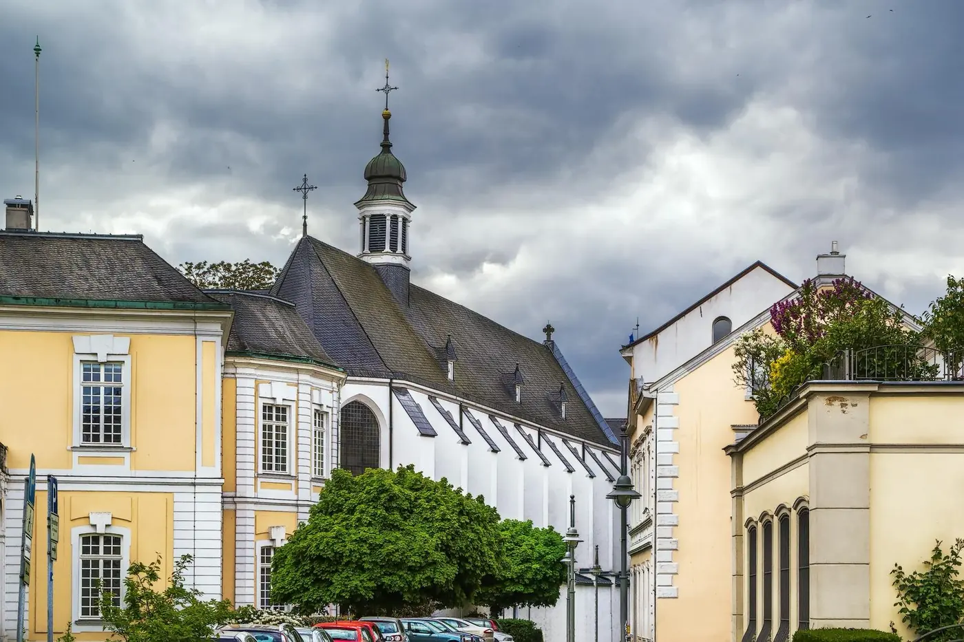 Historische Kirche zwischen hellen Gebäuden unter bewölktem Himmel Historische Kirche zwischen hellen Gebäuden unter bewölktem Himmel