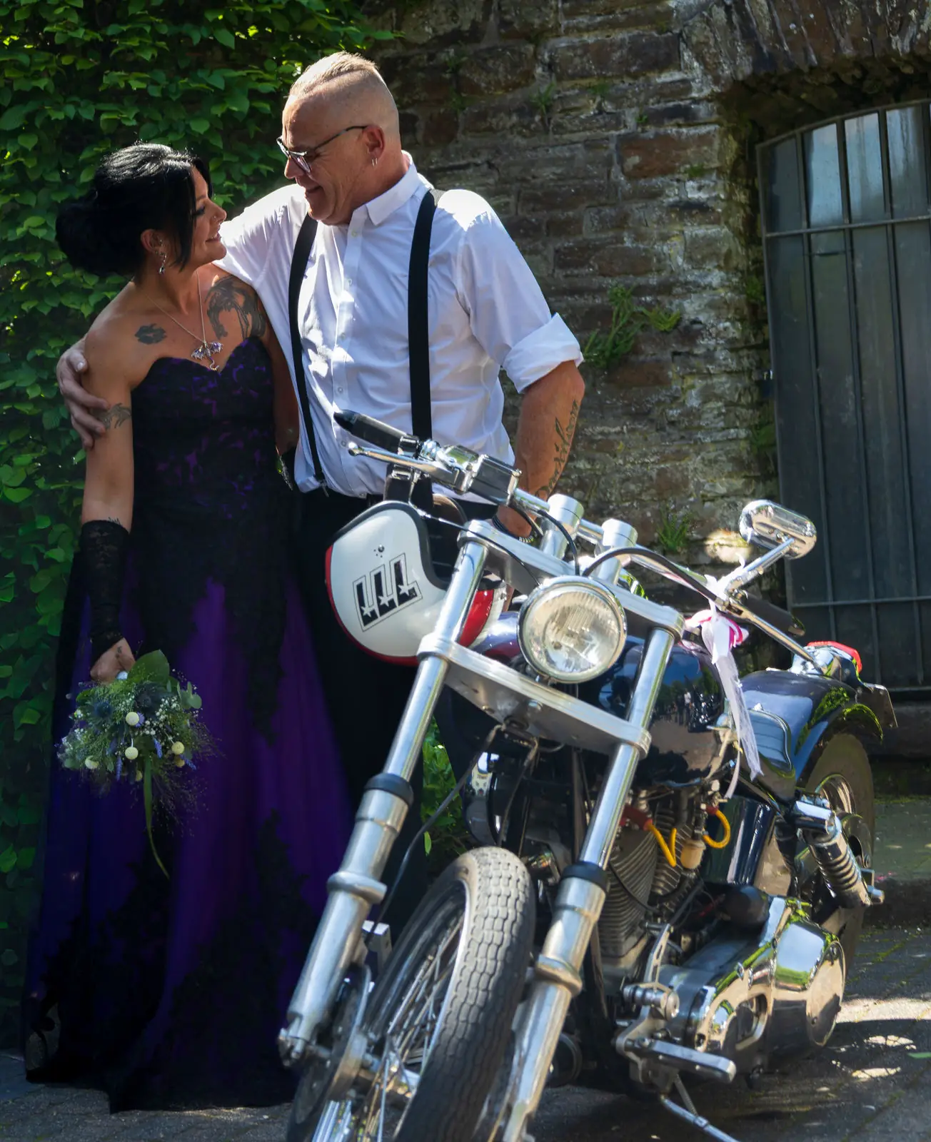 Brautpaar mit Motorrad vor einer Bruchsteinmauer