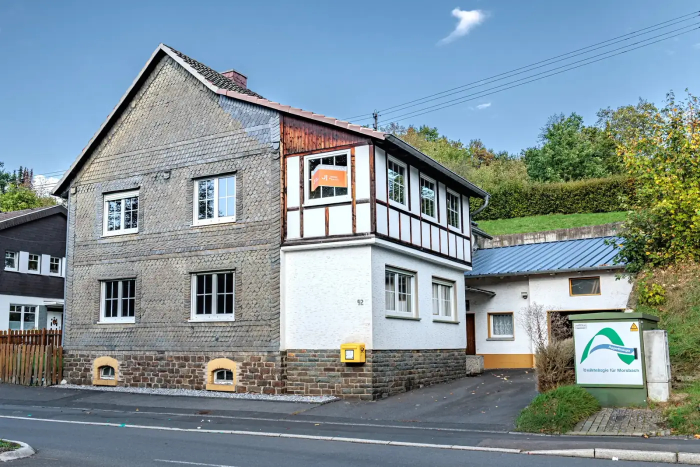 Straßenansicht des Fachwerkhauses mit Schieferfassade, Garage und Verkaufsschild in Morsbach Straßenansicht des Fachwerkhauses mit Schieferfassade, Garage und Verkaufsschild in Morsbach
