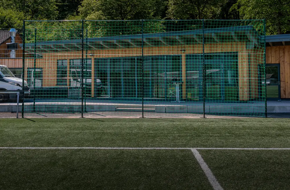 Vereinsheim hinter dem Ballfangnetz eines Kunstrasenplatzes Vereinsheim hinter dem Ballfangnetz eines Kunstrasenplatzes